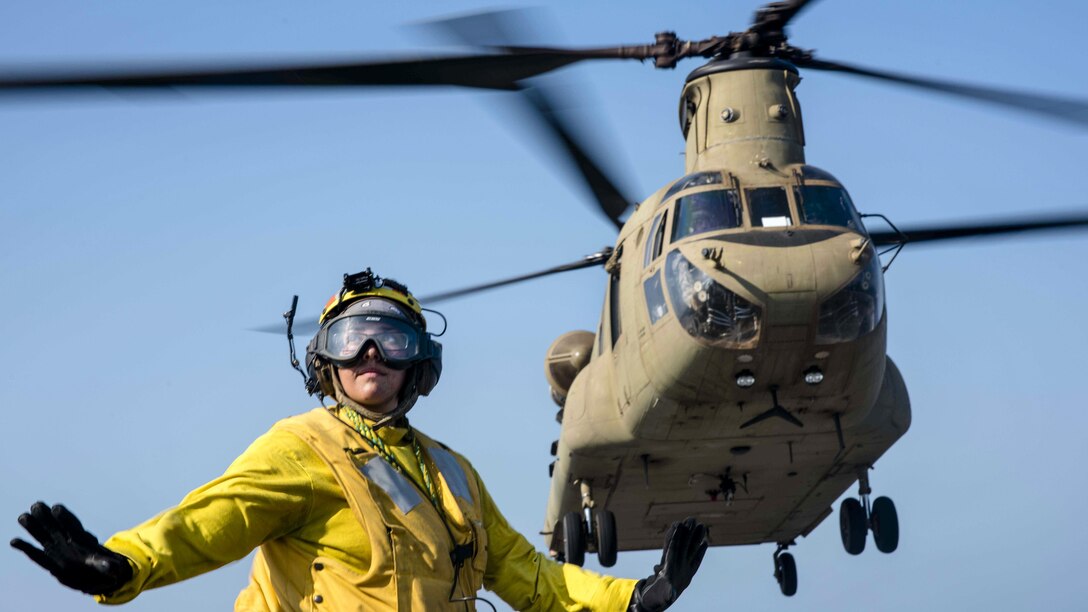 Navy Petty Officer 3rd Class Julia Valles signals to personnel to stand clear as an Army CH-47F Chinook helicopter takes off from the USS Green Bay during Cobra Gold 2017 in the Gulf of Thailand, Feb. 21, 2017. The exercise aims to strengthen engagement in the region. Valles is an aviation boatswain’s mate (handling). Navy photo by Petty Officer 1st Class Chris Williamson 