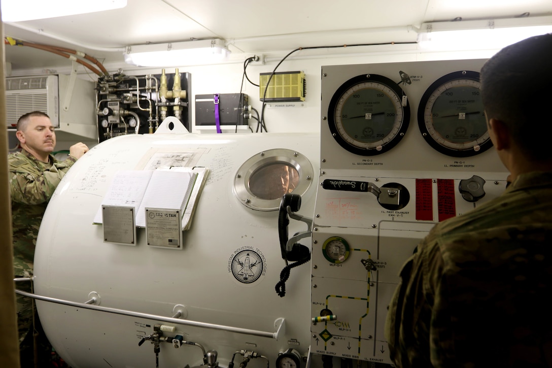 Master Diver 1st Sgt. Tyler Dodd, with the 511th Engineer Dive Detachment out of Fort Eustis, Va., oversees training of the Standard Navy Double Lock Recompression Chamber System while salvage diver Spc. Nathaniel Marquez works the control console, Kuwait Naval Base, Kuwait, Feb. 13, 2017. The training is to give 511th Soldiers hands on training in equipment operation, Soldier advancement and to help a Soldier with an injury sustained during a previous training exercise.