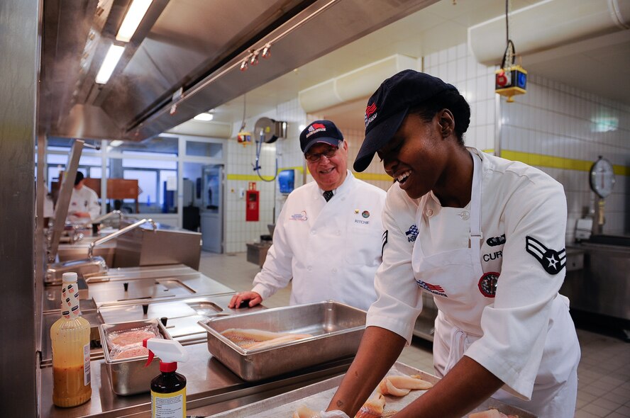 Airman 1st Class Chante Curtis, 786th Force Support Squadron services apprentice, shows Harold Ritchie, Ritchie International principal and hospitality consultant, how she folds fish for presentation during an inspection for the 61st Annual Hennessy Trophy Awards Program at Lindberghof Dining Facility on Kapaun Air Station, Germany, Feb. 21, 2017. This is the third year that the 786th FSS has been nominated for the Hennessy award. (U.S. Air Force photo by Airman 1st Class Savannah L. Waters)