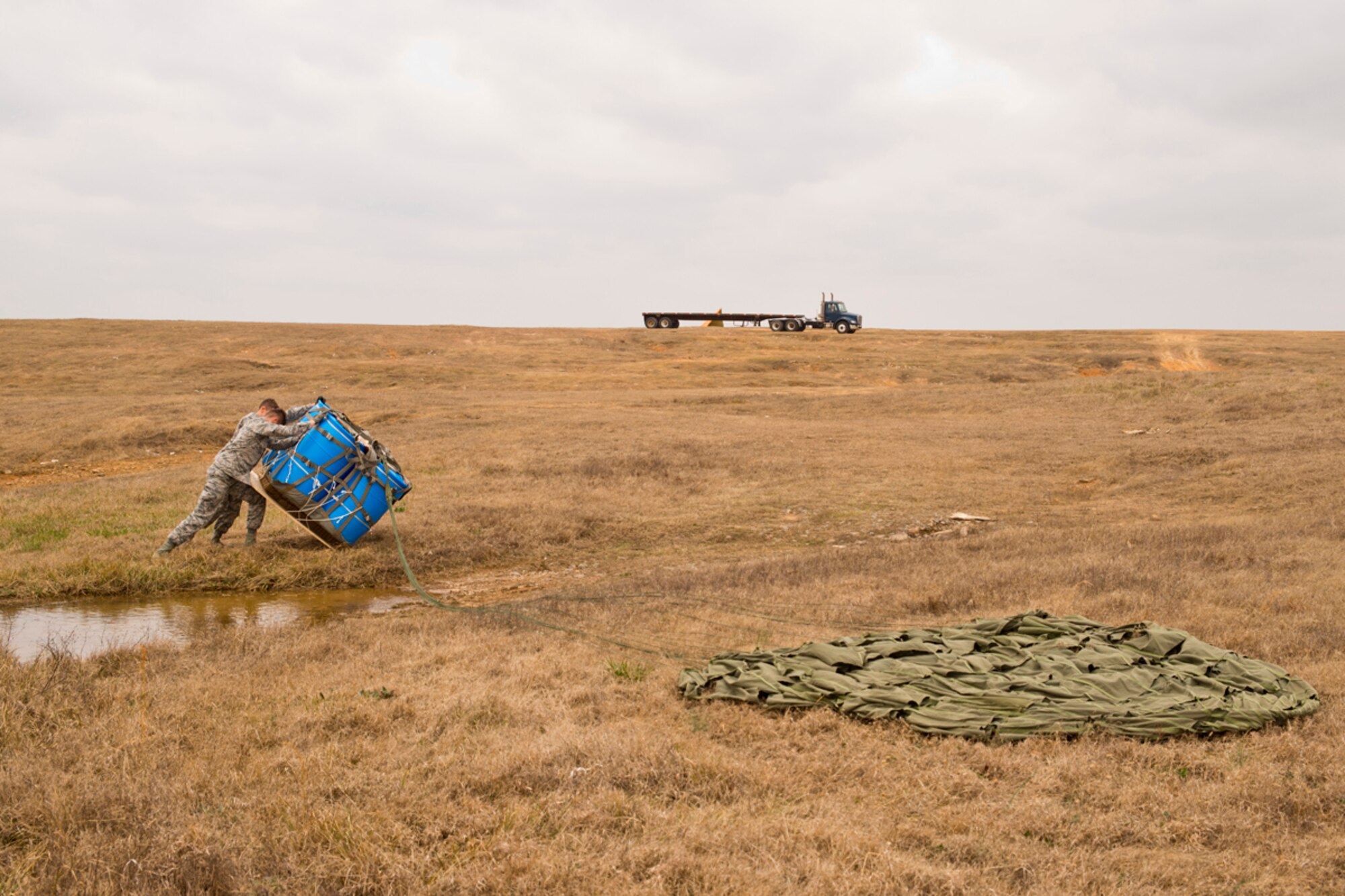 U.S. Air Force Airmen from the 19th Logistics Readiness Squadron roll over a water barrel container delivery system (CDS) at Black Jack Drop Zone Feb. 11, 2017, near Beebe, Ark. While the water barrels drain, the Airmen recover the 26-foot G-12 Cargo Parachute before loading the entire bundle on to a tractor trailer for the return trip to Little Rock Air Force Base. (U.S. Air Force photo by Master Sgt. Jeff Walston/Released)