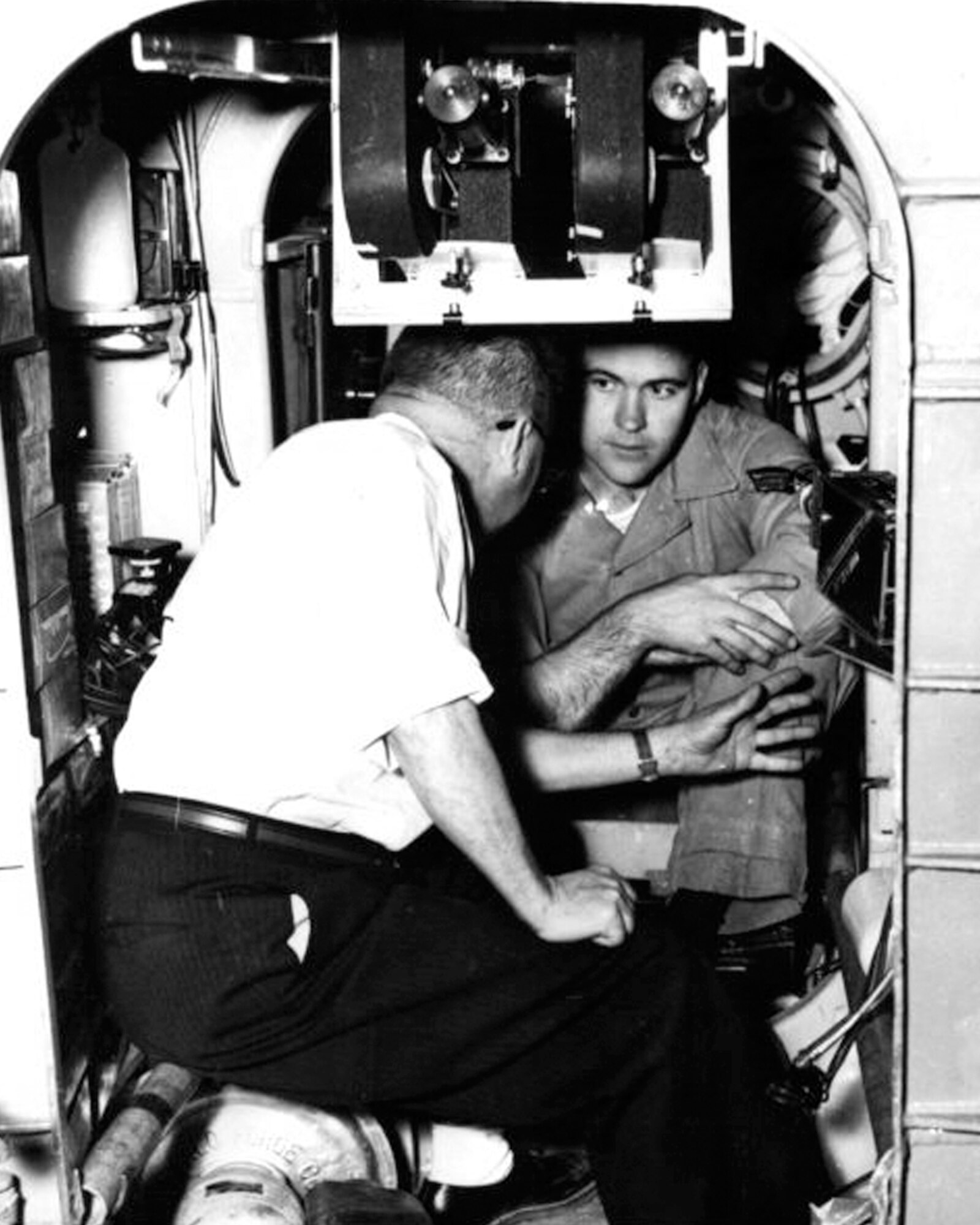 Airman 1st Class Donald G. Farrell, talks with Fenten Duepner, an electronic engineer at the Air Force School of Aviation Medicine, during a pre-ascension briefing at Randolph Air Force Base. Farrell is inside the small shell in which he began a seven-day journey into the unknown on Feb. 9, 1958. The space cabin is designed to duplicate the conditions Farrell might encounter if he were on a trip to the moon. 

Photo Credit, United Press, Feb. 9, 1958
