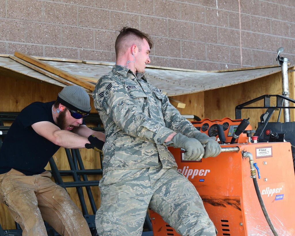 Senior Airman Justin Smith and Mr. Jacob Stahl, 460th Civil Engineering Squadron heavy equipment operators, work to realign machinery used to cut into the cement Feb. 17, 2017 at a dig site on Buckley Air Force Base, Colo. The alignment of the machine is crucial to ensure the lines are straight. (U.S. Air Force photo by Airman 1st Class Jessica A. Huggins/Released)
