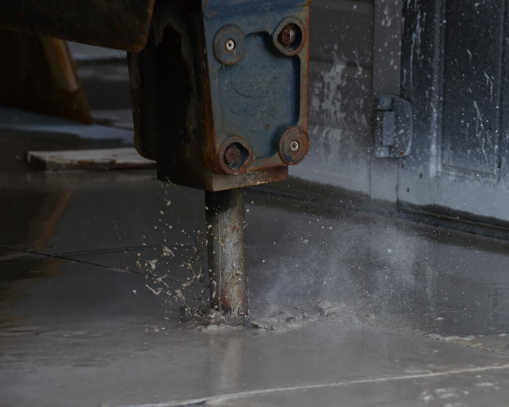 The hydraulic attachment of a Bobcat machine digs a whole into the concrete Feb. 17, 2017 on Buckley Air Force Base, Colo. This is one of the first steps in the process of fixing a pipe leak. (U.S. Air Force photo by Airman 1st Class Jessica A. Huggins/Released)