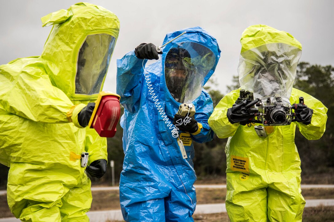 Three Airmen in protective suits use instruments to detect hazardous materials.