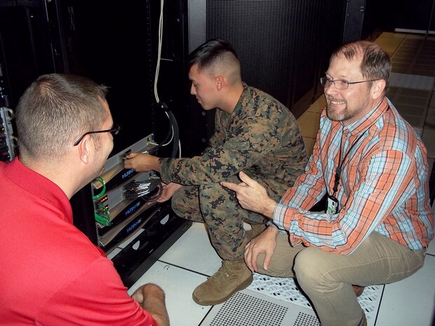 Jason Hessler (left) and Andy Collison (right), Automated Message Handling System support engineers, train a Marine from Marine Corps Installations East G-6 on the Hyper-Converged Infrastructure system Nov. 9, aboard Camp Lejeune, North Carolina. HCI is a virtualization solution that replaces traditional servers, and combines storage and compute functions into a single machine to save cost, energy and space. Marine Corps Systems Command’s Information Systems and Infrastructure recently installed the technology at Camp Lejeune, North Carolina, and Camp Pendleton, California, to support Organizational Messaging Service, which is used to send operational and administrative messages across the Corps. (Courtesy photo)