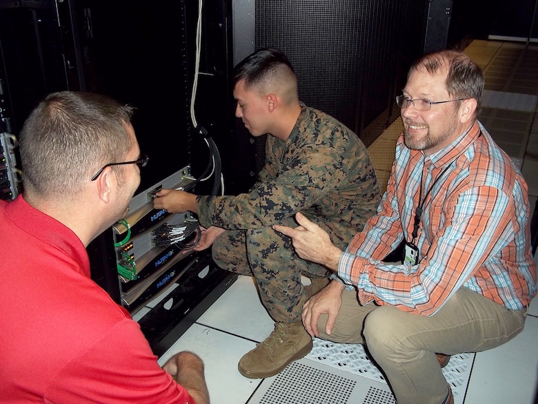 Jason Hessler (left) and Andy Collison (right), Automated Message Handling System support engineers, train a Marine from Marine Corps Installations East G-6 on the Hyper-Converged Infrastructure system Nov. 9, aboard Camp Lejeune, North Carolina. HCI is a virtualization solution that replaces traditional servers, and combines storage and compute functions into a single machine to save cost, energy and space. Marine Corps Systems Command’s Information Systems and Infrastructure recently installed the technology at Camp Lejeune, North Carolina, and Camp Pendleton, California, to support Organizational Messaging Service, which is used to send operational and administrative messages across the Corps. (Courtesy photo)
