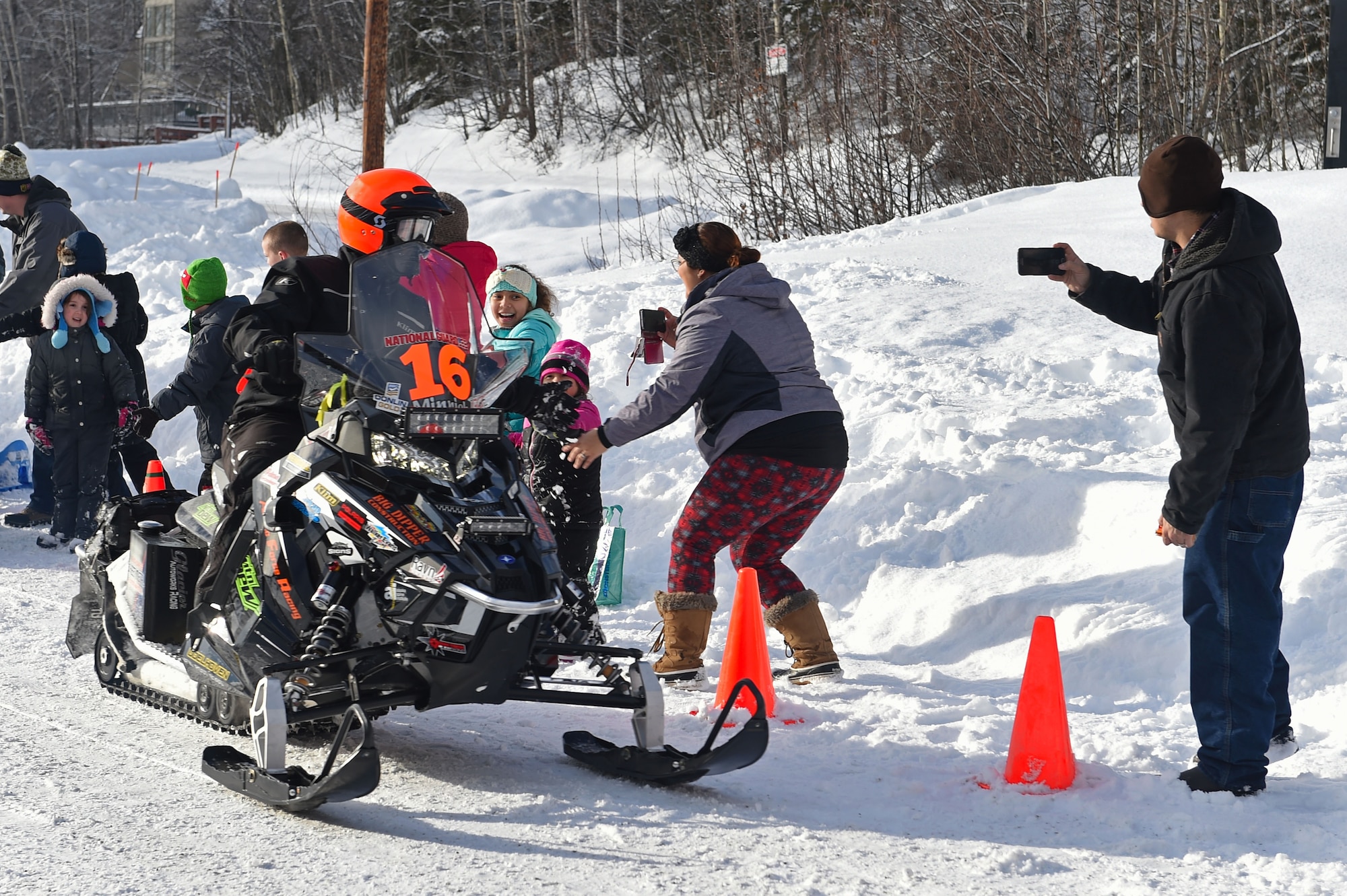 Snowmobile racers high-five military personnel and families as they pass through trails at Joint Base Elmendorf-Richardson, Alaska, during the Iron Dog race Feb. 18, 2017. Iron dog is a long-distance snowmobile race that covers over 2000 miles in Alaska. The trail stretches from Big Lake to Nome, and finishes in Fairbanks. 