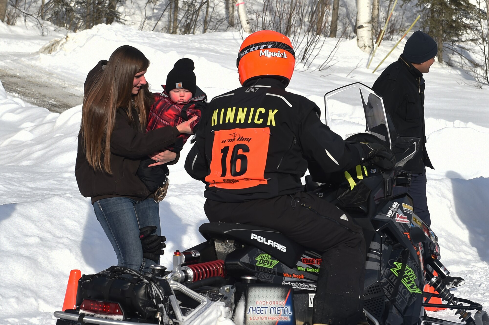 Snowmobile racers high-five military personnel and families as they pass through trails at Joint Base Elmendorf-Richardson, Alaska, during the Iron Dog race Feb. 18, 2017. Iron dog is a long-distance snowmobile race that covers over 2000 miles in Alaska. The trail stretches from Big Lake to Nome, and finishes in Fairbanks. 