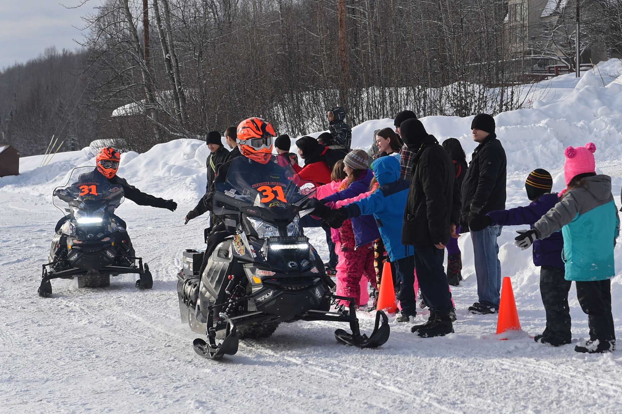 Snowmobile racers high-five military personnel and families as they pass through trails at Joint Base Elmendorf-Richardson, Alaska, during the Iron Dog race Feb. 18, 2017. Iron dog is a long-distance snowmobile race that covers over 2000 miles in Alaska. The trail stretches from Big Lake to Nome, and finishes in Fairbanks.