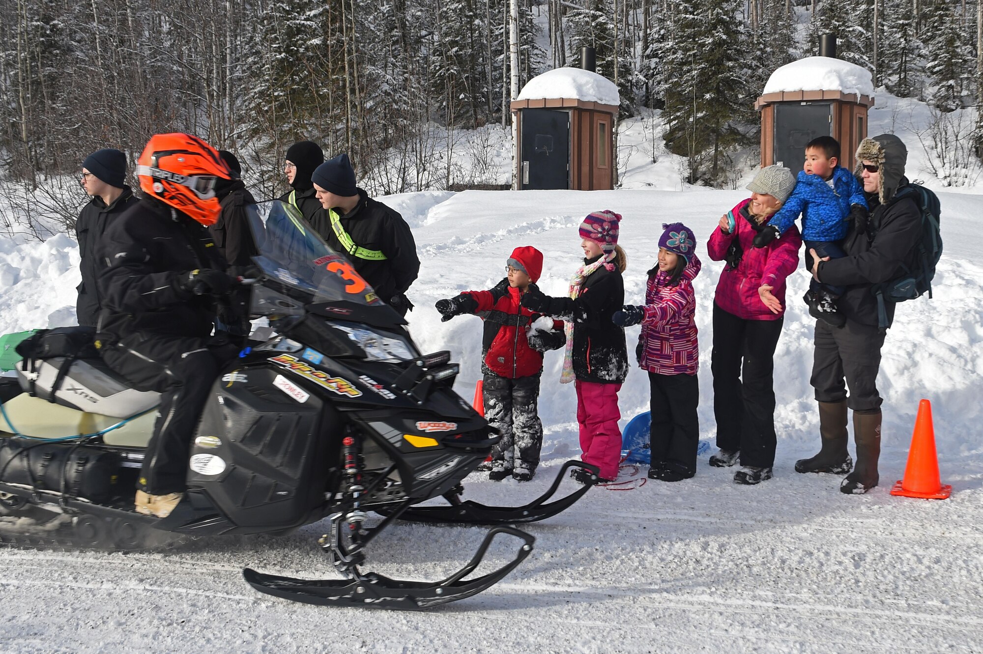 Snowmobile racers high-five military personnel and families as they pass through trails at Joint Base Elmendorf-Richardson, Alaska, during the Iron Dog race Feb. 18, 2017. Iron dog is a long-distance snowmobile race that covers over 2000 miles in Alaska. The trail stretches from Big Lake to Nome, and finishes in Fairbanks. 