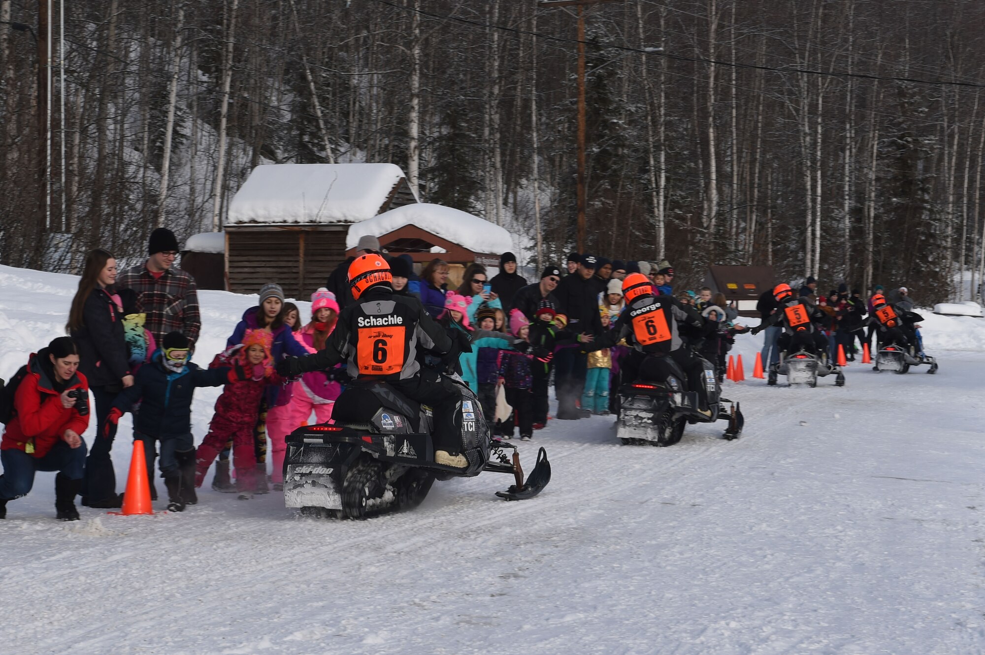 Snowmobile racers high-five military personnel and families as they ride through trails at Joint Base Elmendorf-Richardson, Alaska, during the Iron Dog race Feb. 18, 2017. Race participants cover some of Alaska’s most remote and rugged terrain while confronting some the harshest winter conditions. 