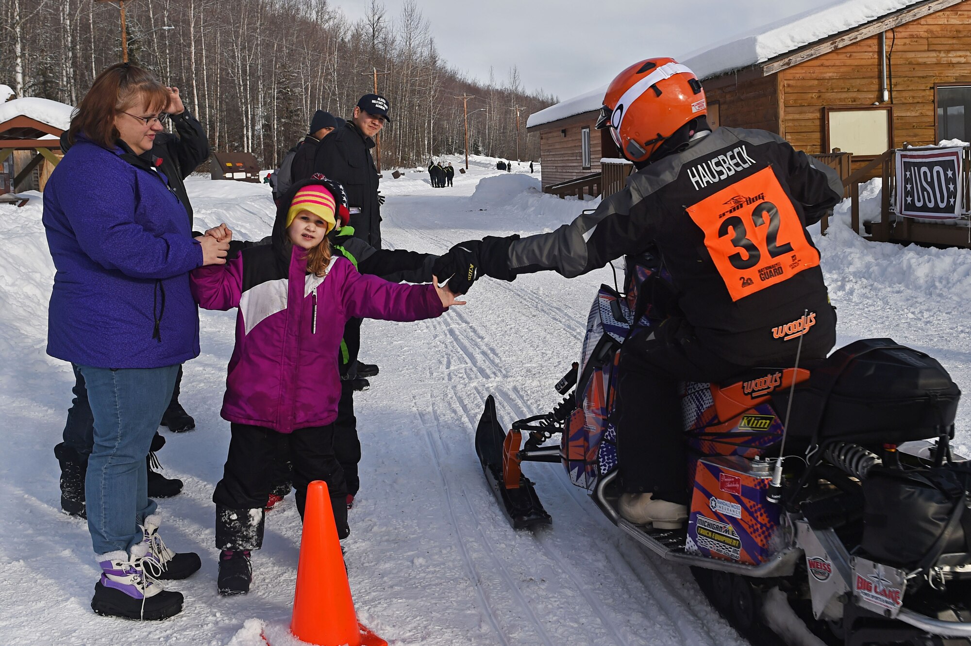 A snowmobile racer high-fives military families while riding through trails at Joint Base Elmendorf-Richardson, Alaska, during the Iron Dog race Feb. 18, 2017. Iron dog is a long-distance snowmobile race that covers over 2000 miles in Alaska. The trail stretches from Big Lake to Nome, and finishes in Fairbanks. 