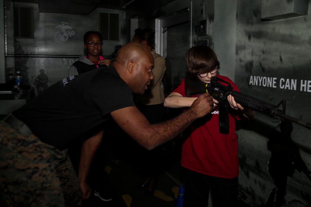 Gunnery Sgt. Maurice S. Sabater, part of the 6th Marine Corps District enhanced marketing vehicle team, assists someone attempting to use the Indoor Simulated Marksmanship Training program at the Central Intercollegiate Athletic Association (CIAA) Fan Fest at the Charlotte Convention Center on Feb. 23, 2017. The Marines take part in the Fan Fest at the CIAA to help spread awareness and inform others of the opportunities the Marine Corps can provide. The Fan Fest assists recruiters by offering them different tools to reach students across the state. (U.S. Marine Corps photo by Lance Cpl. Jack A. E. Rigsby/Released)