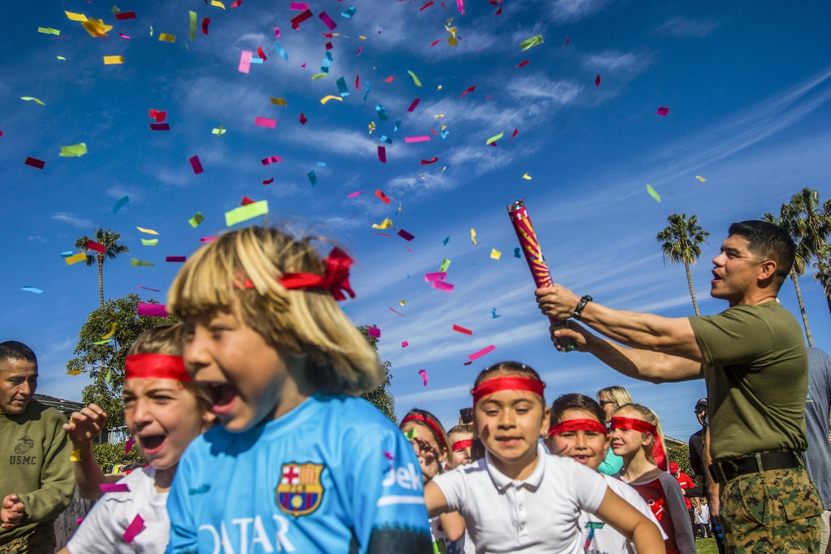 A Marine sets off a confetti cannon as children participate in a running event.