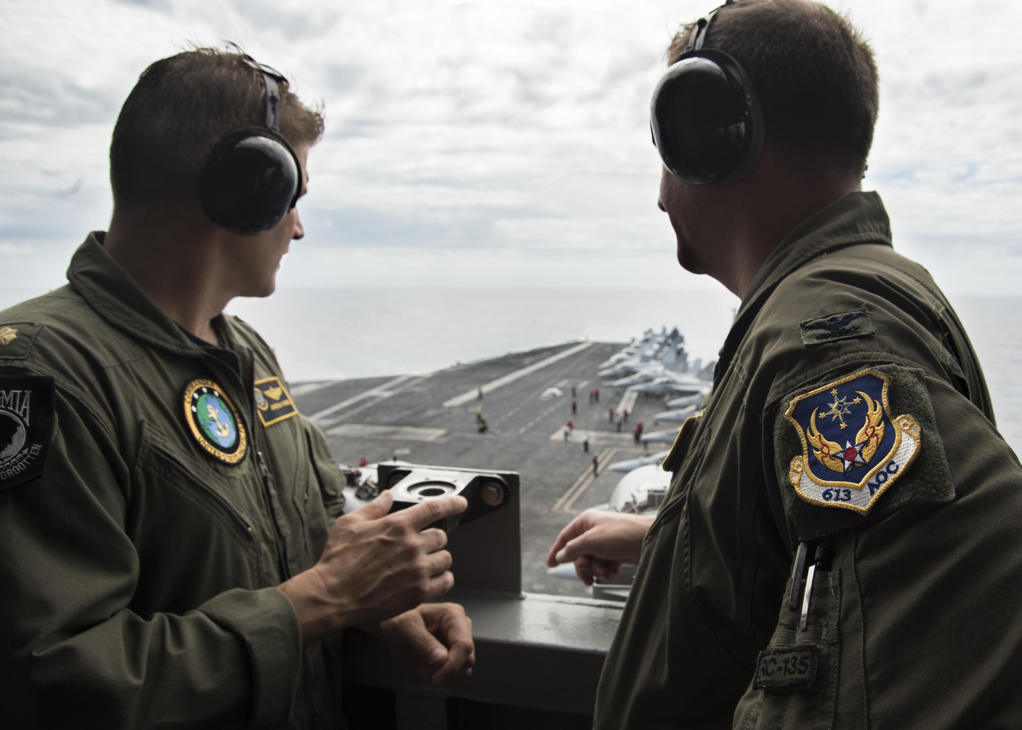 Lt. Cmdr. Jonathan Pohnel, left, Pacific Fleet Liaison Naval Officer, and U.S. Air Force Col. Doug Rice, Chief of the Combat Plans Division at 613th Air Operations Center (AOC), Joint Base Pearl Harbor-Hickam, Hawaii, view flight operations on the aircraft carrier USS Carl Vinson (CVN 70). A four-member team of representatives from the AOC joined the crew of USS Carl Vinson to help bridge the efforts between the AOC and Navy Units while transiting the Pacific area of responsibility. The Carl Vinson Carrier Strike Group is on a regularly scheduled Western Pacific deployment as part of the U.S. Pacific Fleet-led initiative to extend the command and control functions of U.S. 3rd Fleet. U.S Navy aircraft carrier strike groups have patrolled the Indo-Asia-Pacific regularly and routinely for more than 70 years. (U.S. Navy Photo by Seaman Jake Cannady)