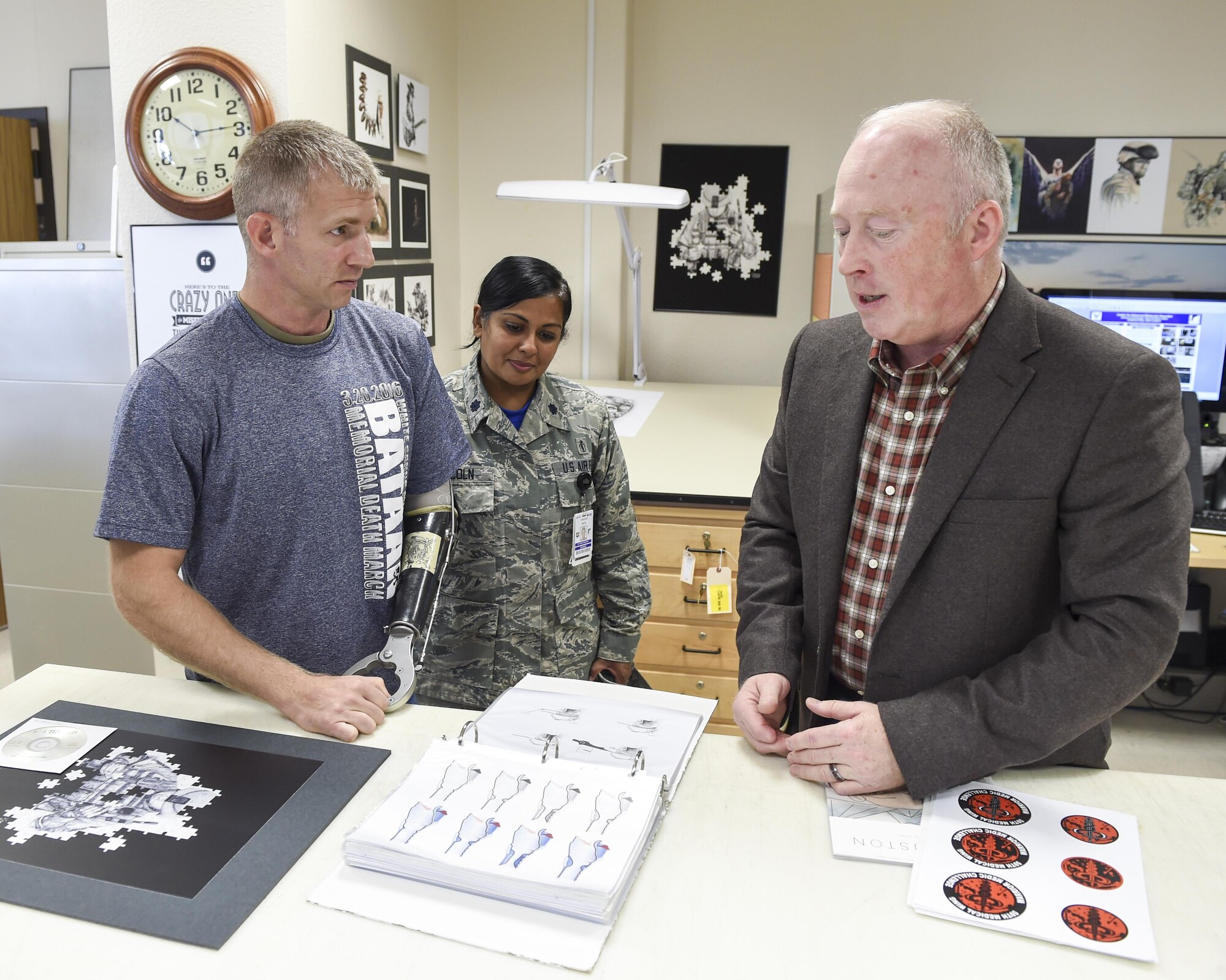 Robert Shelley, 59th Medical Wing graphics illustrator, explains some of the projects the medical illustrations department has done to Lt. Col. Kenneth Dwyer, patient and Special Forces officer assigned to U.S. Army 1st Special Forces Command (Airborne), and Lt. Col. (Dr.) Ketu Lincoln, 59th MDW maxillofacial prosthodontic fellow, at Wilford Hall Ambulatory Surgical Center on Joint Base San Antonio-Lackland, Texas, Nov. 18, 2016. Shelley also sketched the unit crest for Dwyer's prosthetic eye. (U.S. Air Force photo/Staff Sgt. Michael Ellis)
