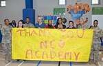 (From left) Sgt. 1st Class Roberta Stevens, Vanessa Fo-Norton, Sgt, 1st Class Antonio Young, Staff Sgt. Brady Kornelis, Karen Archondisis, Danielle Smith, Mariana Ruiz, Command Sgt. Maj. Napoleon Noguerapayan and 1st Sgt. Thadenia Leach hold up a sign from students at Smith Elementary School thnaking the Non-Commissioned Officer Academy at Joint Base San Antonio-Fort Sam Houston for donated school supplies Dec. 16, 2016.