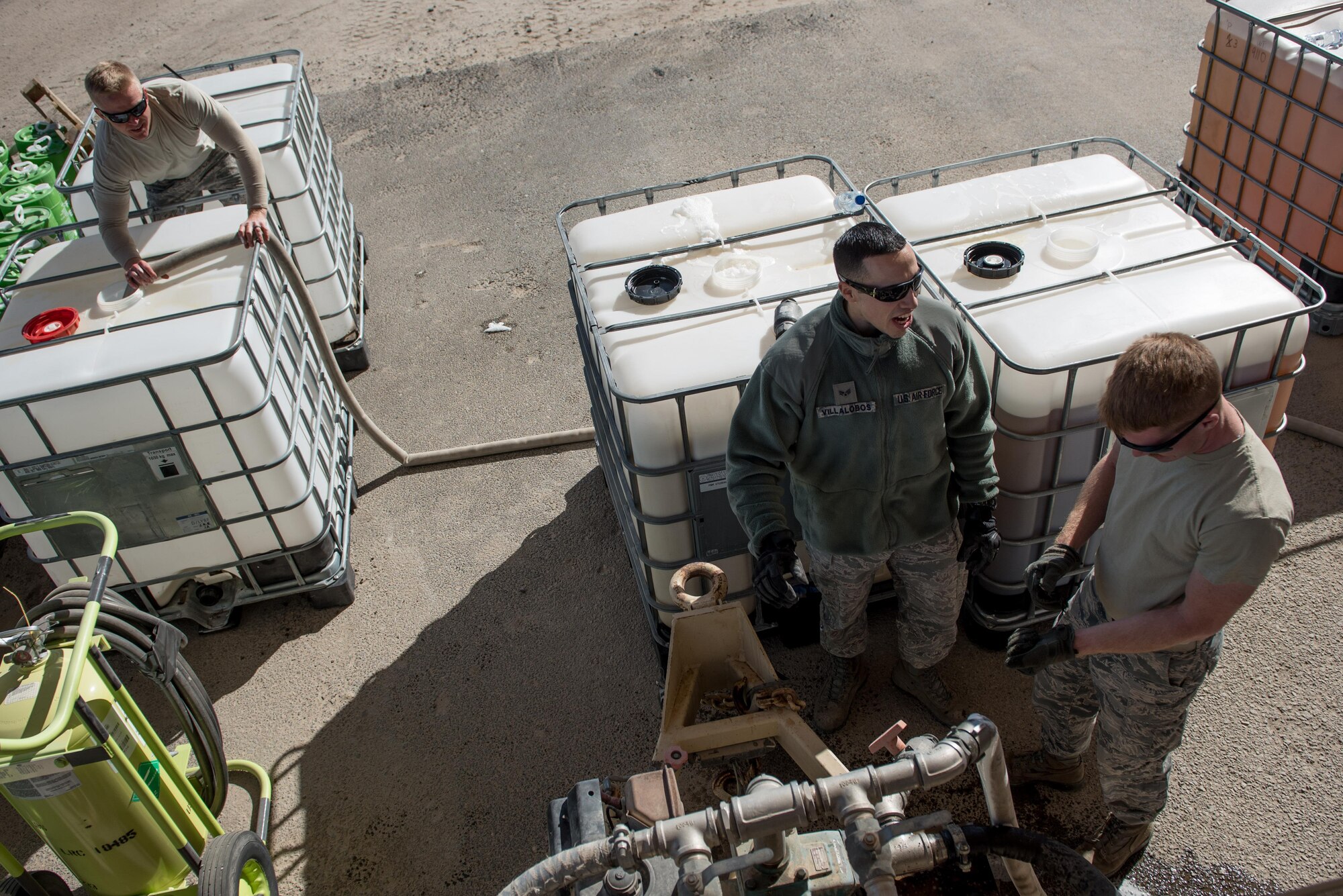 Tech. Sgt. Jason Demoss, 407th Expeditionary Civil Engineer Squadron assistant chief of firefighting operations (left); Senior Airman Francisco Villalobos (center) and Staff Sgt. Clinton Manus, both 407th ECES firefighters,squeegees transfer fire retardant from a foam trailer with at the 407th Air Expeditionary Group, Jan. 6, 2016. The unit switched to new fire retardant foam in their foam trailer, and six crash vehicles.  (U.S. Air Force photo/Master Sgt. Benjamin Wilson)(Released)