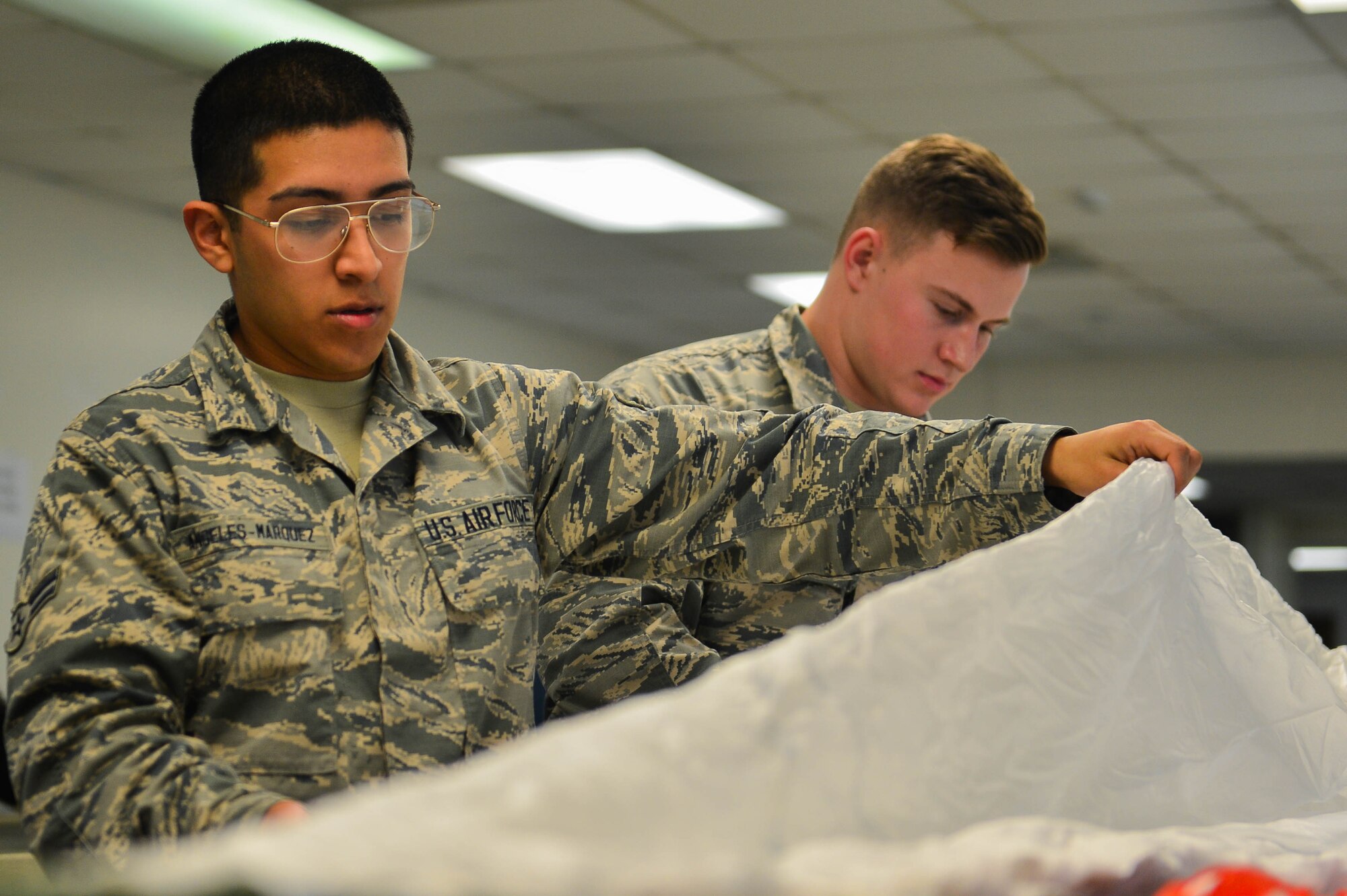 U.S. Air Force Airmen 1st Class Carlos Angeles-Marquez, left, and Devin Daniels, right, 20th Operations Support Squadron aircrew flight equipment journeymen, examine a parachute for damage at Shaw Air Force Base, S.C., Jan. 14, 2017. Parachutes are routinely inspected and repaired to meet all safety specifications. (U.S. Air Force photo by Airman 1st Class Christopher Maldonado)