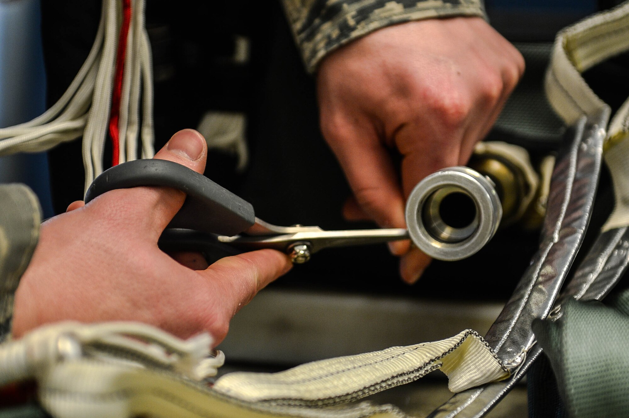 U.S. Air Force Airman 1st Class Devin Daniels, 20th Operations Support Squadron aircrew flight equipment journeyman, uses scissors to cut a protective band from a parachute at Shaw Air Force Base, S.C., Jan. 4, 2017. The protective bands of the parachute prevent misfires in the cockpit that may cause injury to the pilot. (U.S. Air Force photo by Airman 1st Class Christopher Maldonado)