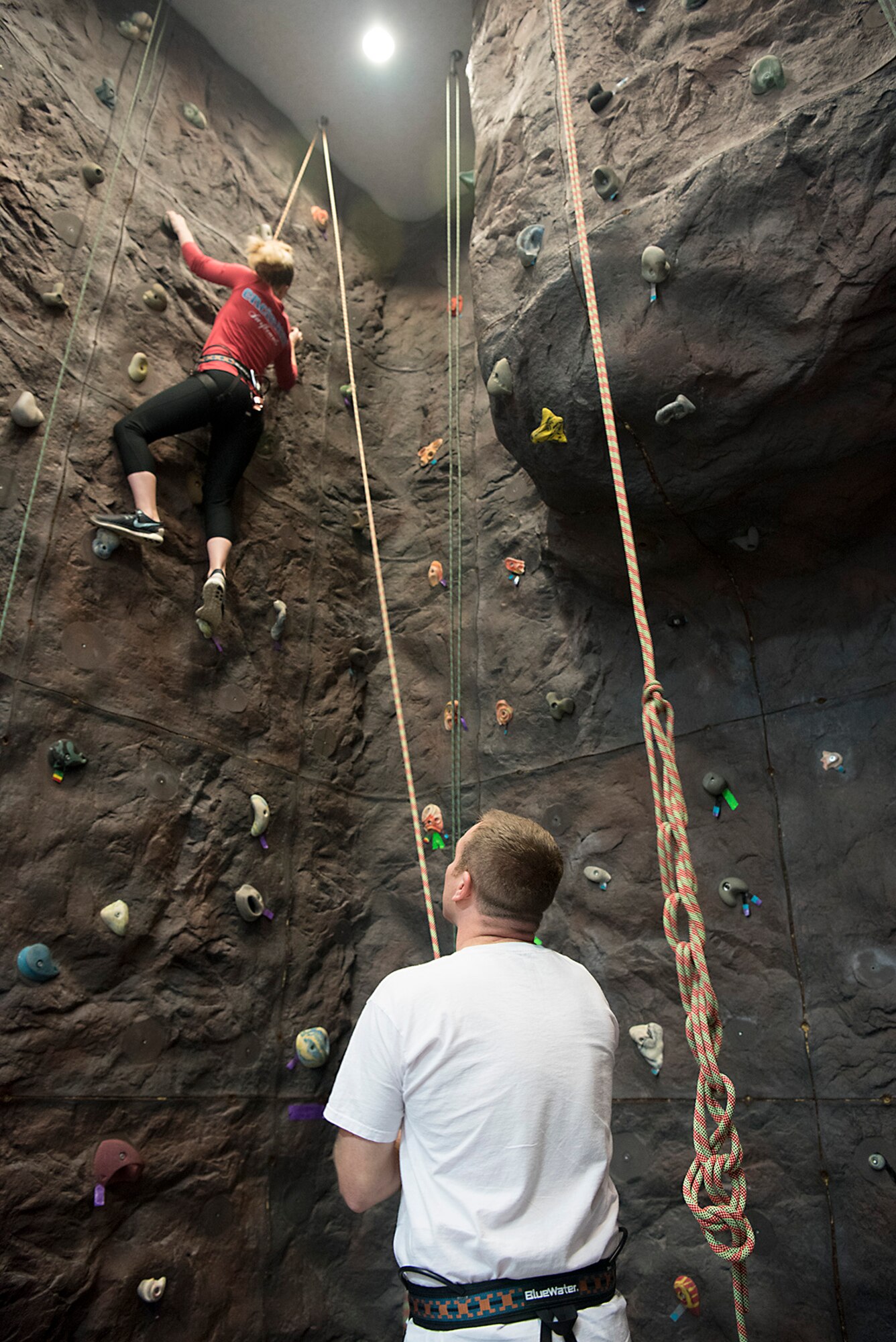 PETERSON AIR FORCE BASE, Colo. – Master Sgt. Jared Rinderer, U.S. Air Force Academy military trainer, belays for his wife, Faith Rinderer, while she climbs the rock wall in the fitness center at Peterson Air Force Base, Colo., Dec. 14, 2016. The rock wall is located in the fitness center behind the free weights room and is available for use by all gym patrons during normal gym hours. All that is required to climb is completion of a certification course which is given twice a month. The climbing varies from bouldering to top rope climbing rated from 5.0 to 5.10. For more information stop by the front desk of the fitness center. (U.S. Air Force photo by Steve Kotecki)