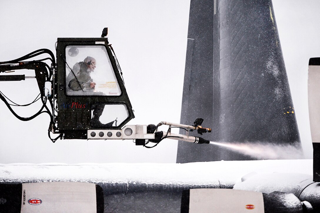 An airman operates a vehicle to de-ice an aircraft.