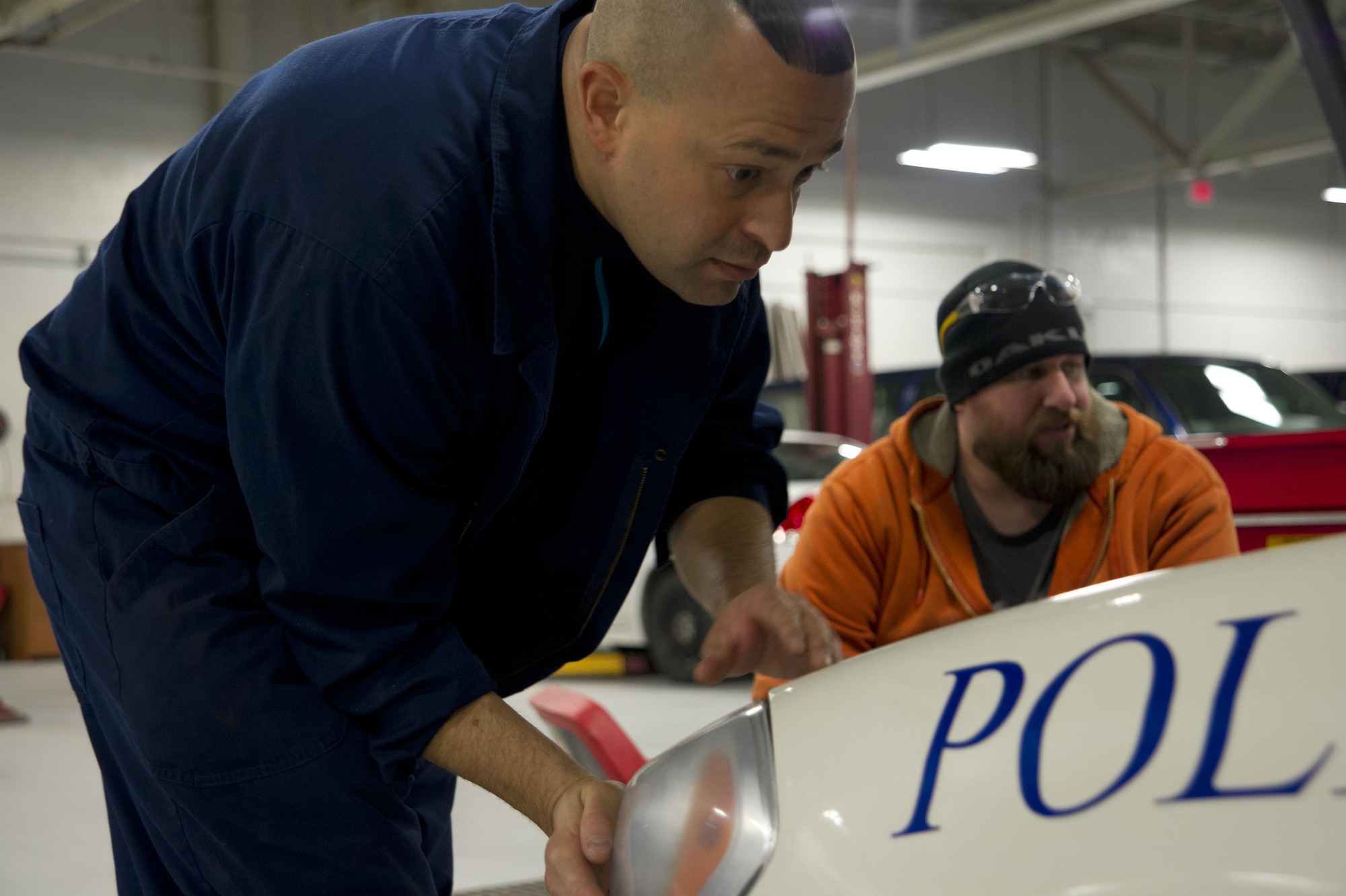 Danny Santana, Data Monitor Systems head mechanic, replaces the headlight on a police cruiser while Brayman "BB" Burnsworth, DMS mechanic, inspects the engine at Grissom Air Reserve Base, Ind., Jan. 4, 2017. The police cruiser had been brought in for multiple heat-related issues which had melted some of its parts. (U.S. Air Force photo/Senior Airman Harrison Withrow)