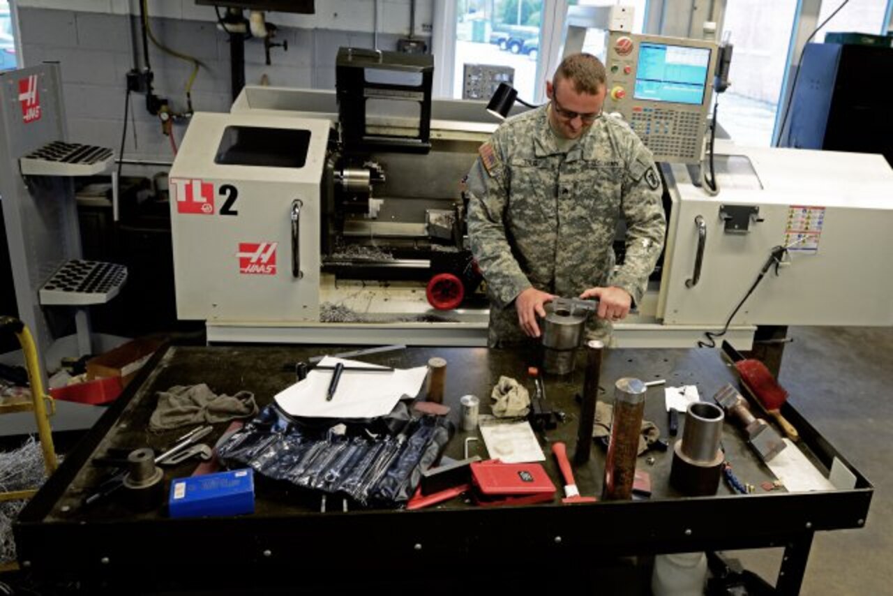 Sgt. Wesley Todd, of La Porte, Indiana, tightens his invention, used to remove the muzzle break from the light towed howitzer, on to a lathe in the machine shop at the at the Combined Support Maintenance Shop in North Riverside, Illinois. The device Todd invented improves Soldier safety and equipment longevity while working on the light towed howitzer. 