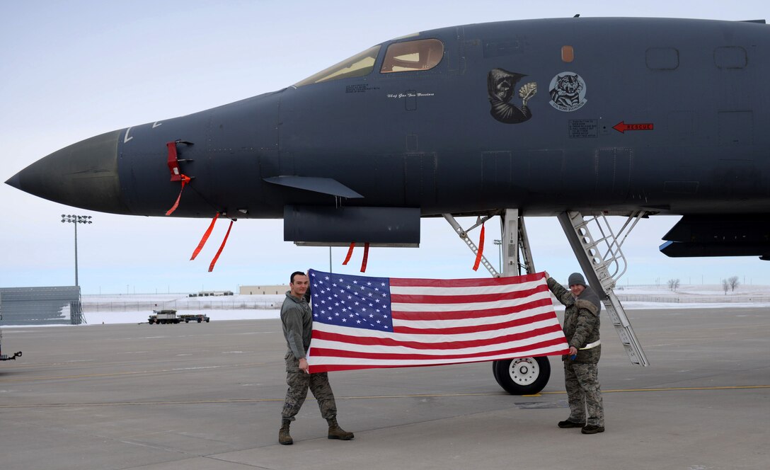 Staff Sgt. Jonathan Balko, an electrical and environmental craftsman assigned to the 28th Aircraft Maintenance Squadron, left, holds up his American flag in front of a B-1 bomber at Ellsworth Air Force Base, S.D., Jan. 4, 2017. Balko first received his flag while on his first deployment to Al Udeid Air Base, Qatar, and since then has taken it to every place he visits, tracking its presence in more than 20 locations. (U.S. Air Force photo by Airman 1st Class Denise M. Jenson)