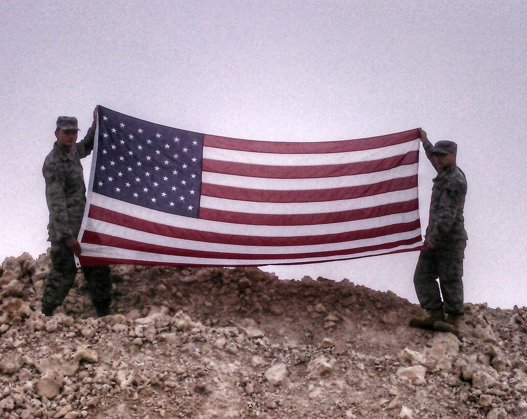 Staff Sgt. Jonathan Balko, an electrical and environmental craftsman assigned to the 28th Aircraft Maintenance Squadron, left, holds up his American flag at a deployed location. From a young age, Balko knew he wanted to have a career related to military aviation. (Courtesy photo)