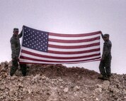 Staff Sgt. Jonathan Balko, an electrical and environmental craftsman assigned to the 28th Aircraft Maintenance Squadron, left, holds up his American flag at a deployed location. From a young age, Balko knew he wanted to have a career related to military aviation. (Courtesy photo)
