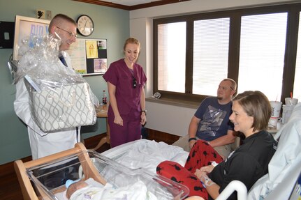 Brig. Gen. Jeffrey Johnson, commander, Brooke Army Medical Center, and BAMC registered nurse Kassandra Garza congratulate and deliver a gift basket to U.S. Army Sgt. Tiffany Curtis, 7210 Medical Support Unit, Fort Sam Houston, Texas, and husband Justin Curtis. They are the proud parents of Lexy Curtis, the first baby born at Brooke Army Medical Center, Jan. 1, 2017. (U.S. Army photo by Robert A. Whetstone/Released)