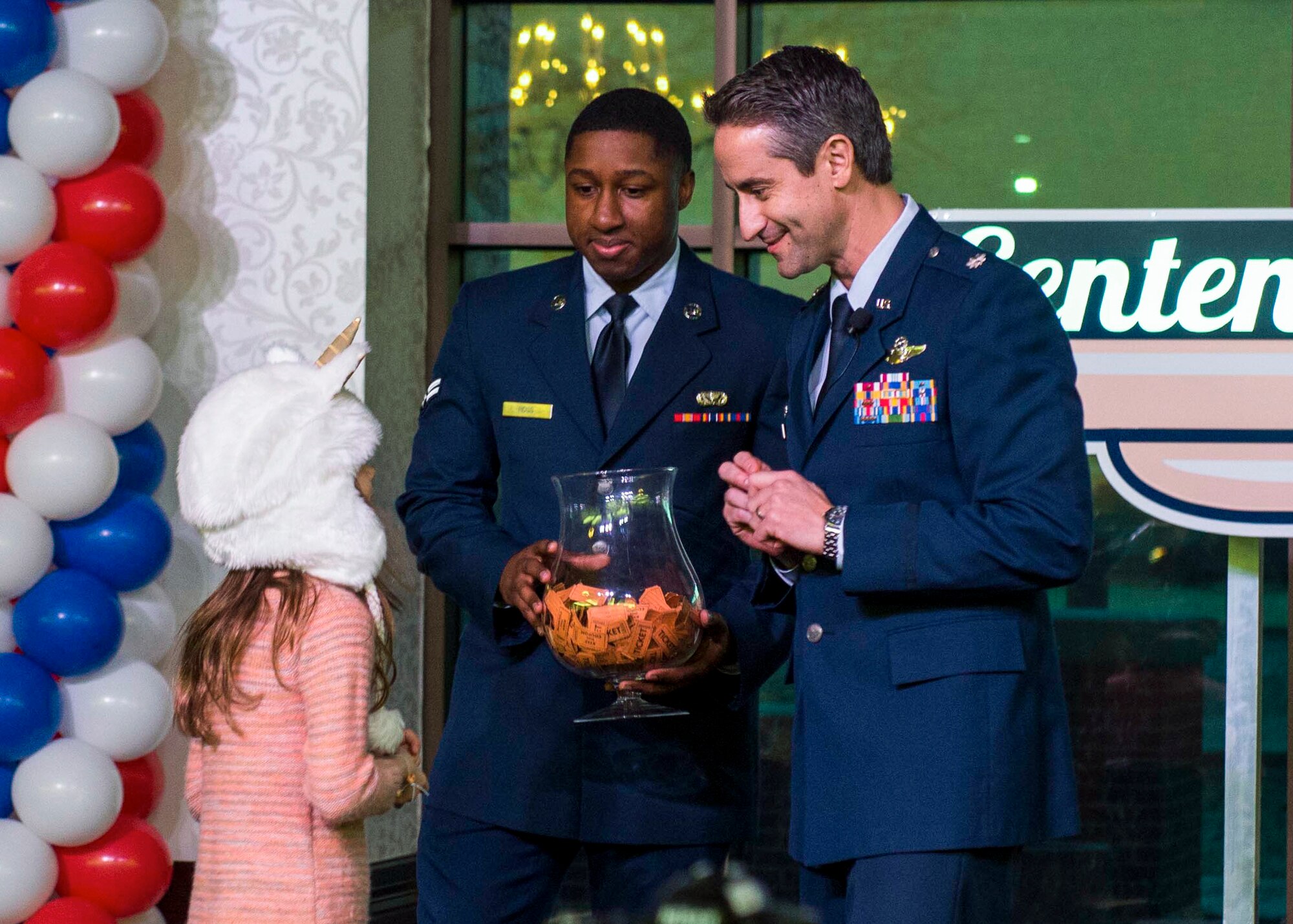 Ashley Carr, the daughter of Angela Carr and Senior Master Sgt. Adam Carr, 375th Comptroller Squadron superintendent, helps Lt. Col. Matthew Getty, 375th Operations Support Squadron, and Airman 1st Class Class Rodney Ross, 375th Force Support Squadron, select a raffle ticket for prizes during the centennial kickoff at the Scott Event Center, Jan. 6, 2017. Getty was the master of the ceremony for the evening. (U.S. Air Force Photo by Senior Airman Megan Friedl)