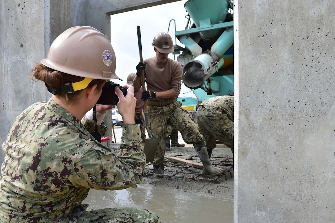 Navy Seaman Emily Manley with Naval Mobile Construction Battalion 5 takes photos of Seabees as they move concrete around the job site at White Beach, Okinawa, Japan, Jan. 10, 2016. The structure they are building will house a generator for the base fire department. NMCB-5 provides general engineering and civil support to Navy, Marine Corps and joint operational forces. Navy photo by Petty Officer 2nd Class Adam Henderson