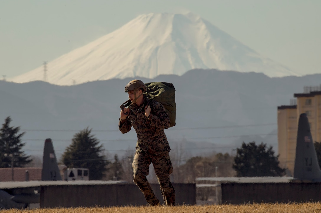 A U.S. Marine from the 3rd Reconnaissance Battalion, 3rd Marine Division, III Marine Expeditionary Force carries his parachute after landing at Yokota Air Base, Japan, Jan. 10, 2017, during Jump Week. The training not only allowed the Marines to practice jumping, but it also allowed the Yokota aircrews to practice flight tactics and timed-package drops. (U.S. Air Force photo by Yasuo Osakabe/Released)