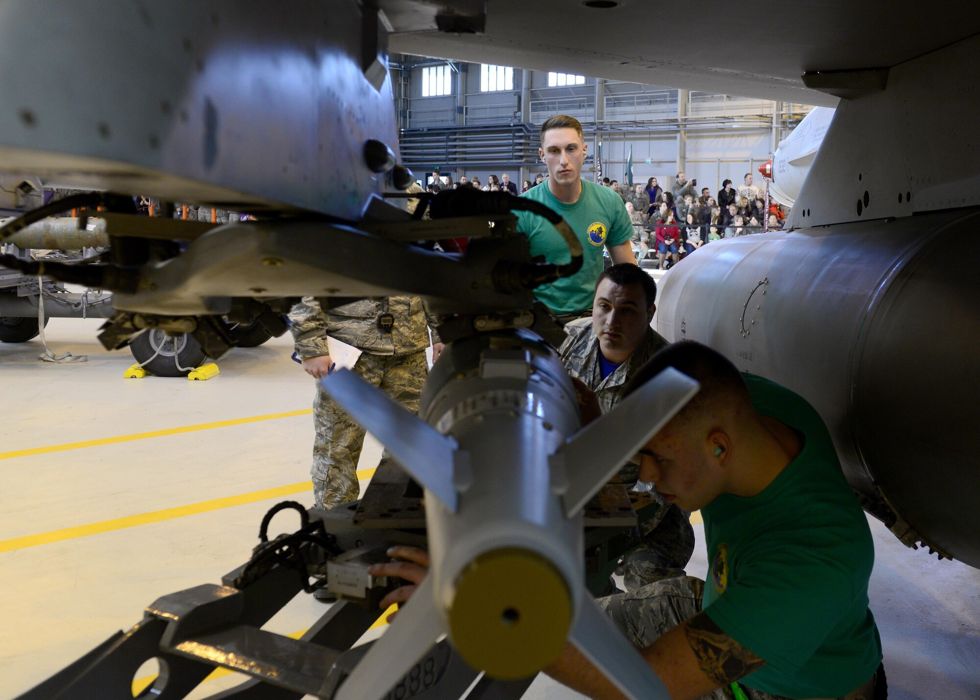 Airman 1st Class Erik Newman, back, 31st Aircraft Maintenance Squadron weapons load crew member, and Staff Sgt. Elijah Duffy, center, load competition judge, watch Staff Sgt. Joshua Walker, front, 31st AMXS weapons load crew chief, install an inert munition during the annual load competition at Aviano Air Base, Italy on Jan. 6, 2016. Each year, the squadron’s top weapons load crew teams compete for the 31st Fighter Wing Best Load Crew of the Year award.  (U.S. Air Force photo by Senior Airman Cary Smith)