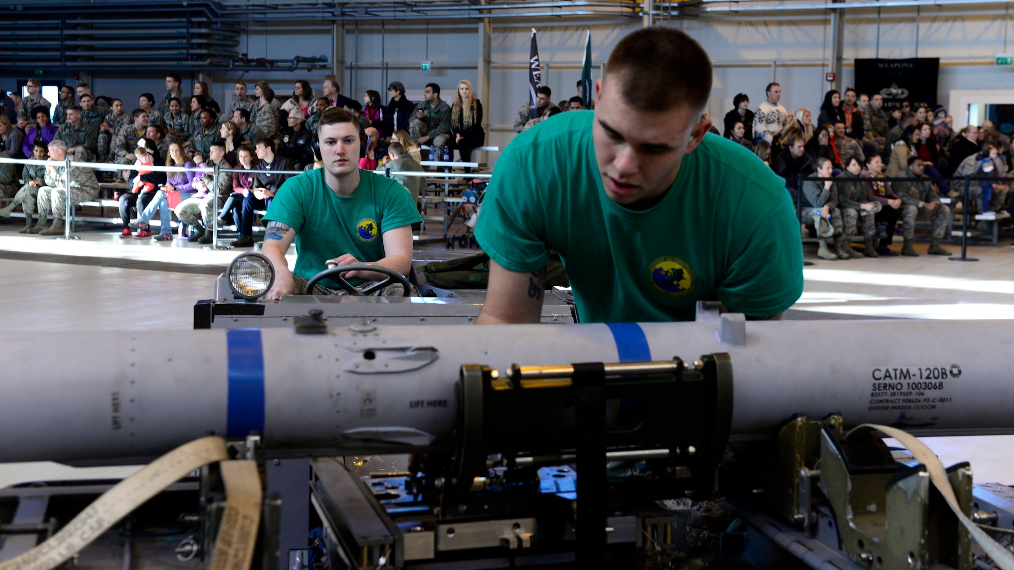 Airman 1st Class Matthew Youngblood, 31st Aircraft Maintenance Squadron weapons load crew member, and Staff Sgt. Joshua Walker, 31st AMXS weapons load crew chief, attach an inert munition to a transportation cart during the annual load competition at Aviano Air Base, Italy on Jan. 6, 2016. The three, 3-person teams were judged on their job knowledge, dress and appearance, and munitions load performance. (U.S. Air Force photo by Senior Airman Cary Smith)