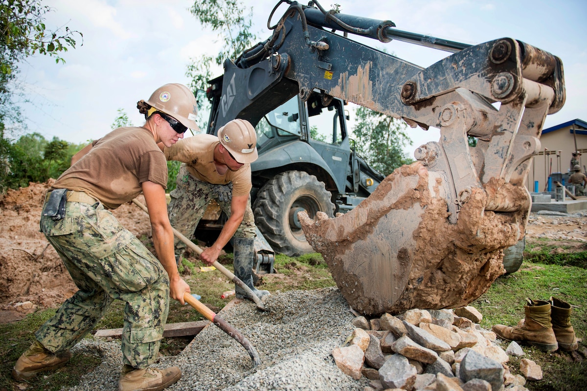 Sailors shovel gravel for a five-stall bathroom they are building for a school.