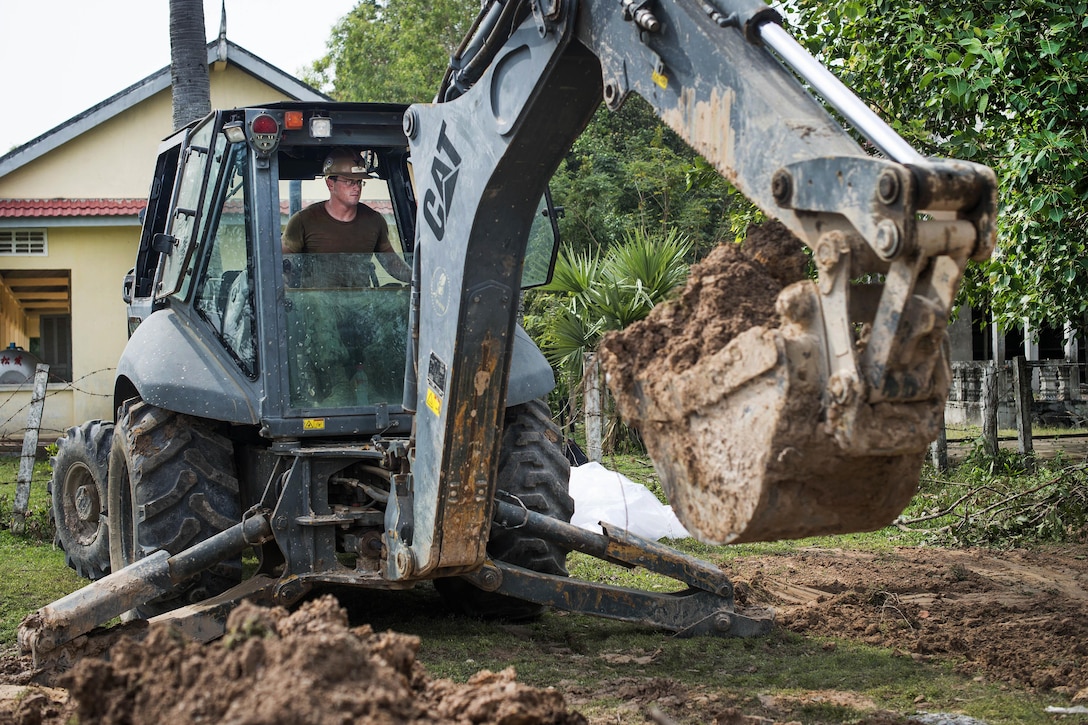 Navy Petty Officer 3rd Class Charles Lutho uses a backhoe to scoop up dirt to cover pipes for a five-stall bathroom project for the Sromo Primary School in Svay Rieng province, Cambodia, Jan. 11, 2017. Lutho is an equipment operator assigned to Naval Mobile Construction Battalion 5. Navy photo by Petty Officer 1st Class Benjamin A. Lewis