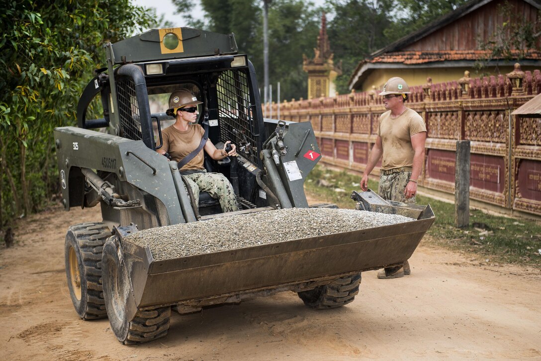 Navy Petty Officer 3rd Class Charles Luthor, right, ground-guides for Petty Officer 2nd Class Viktoria Thompson to get a load of gravel for a five-stall bathroom they are building for the Sromo Primary School in Svay Rieng province, Cambodia, Jan. 11, 2017. Luthor is an equipment operator and Thompson is an engineer assigned to Naval Mobile Construction Battalion 5. Navy photo by Petty Officer 1st Class Benjamin A. Lewis