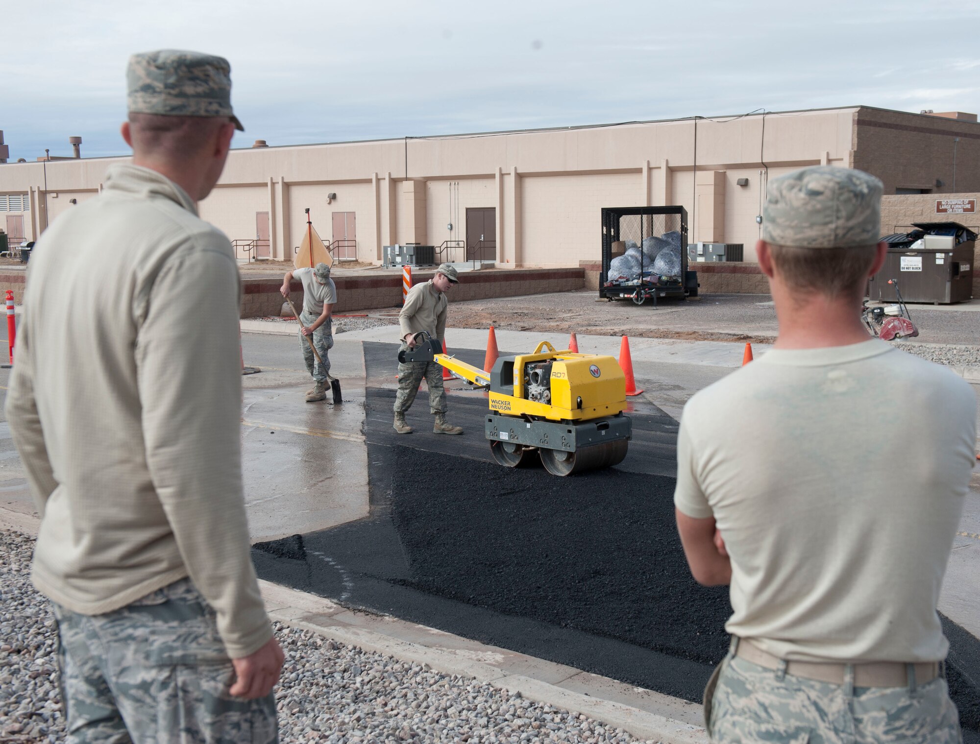Senior Airman Alec Bacon and Senior Airman Jordan Lechner, Pavement and Equipment craftsmen, assigned to the 49th Civil Engineer Squadron, compact fresh asphalt with a heavy roller at Holloman Air Force Base, N.M., January 17, 2017. After the broken utility line was replaced, the CE team came in and backfilled the hole topping it off with fresh asphalt. A utility break occurred under the roadway causing for the 49th CES to quickly respond and fix the problem. (U.S. Air Force photo by Airman Ilyana A. Escalona)