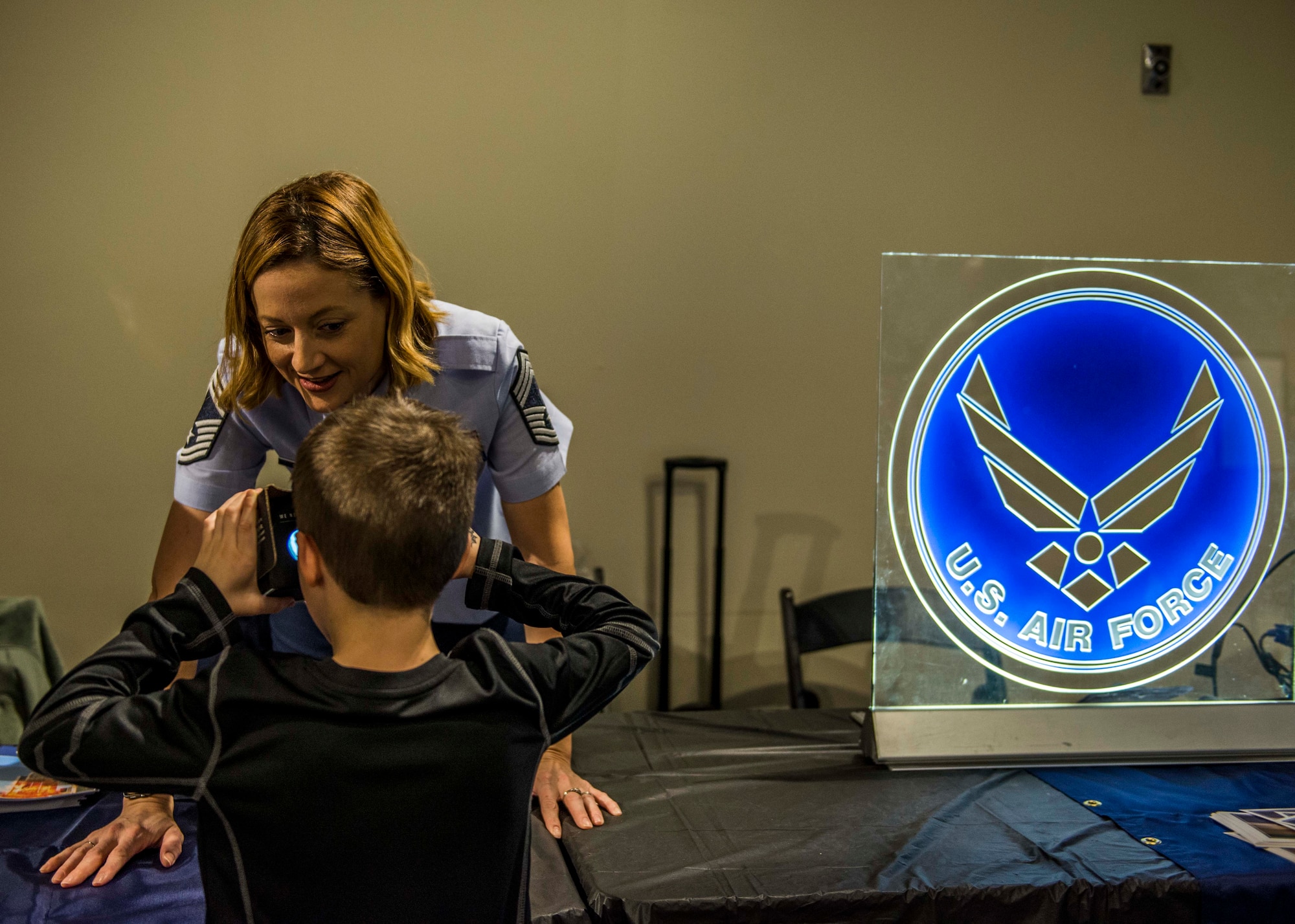 Chief Master Sgt. Diane Slazinik, 375th Communications Group superintendent, asks a visitor what they’re experiencing while they use the Google cardboard virtual reality box to see what it looks like to jump out of a plane as a paratrooper. (U.S. Air Force photo by Staff Sgt. Jodi Martinez)