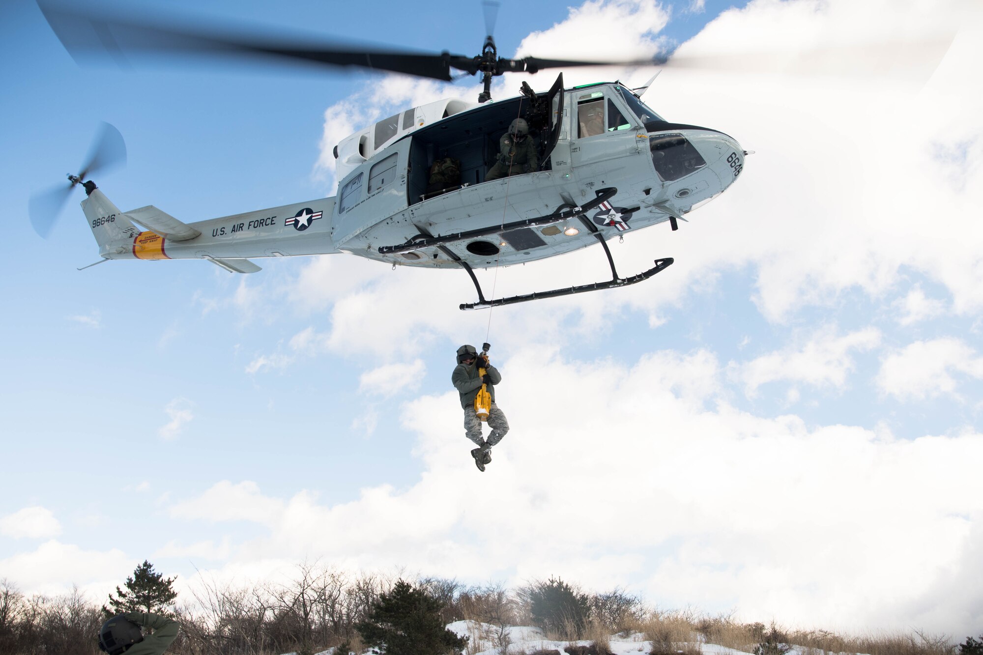 Tech. Sgt. Michael Wright, 459th Airlift Squadron special mission aviator evaluator, holds onto the cable as Master Sgt. Antonio Gueits, 374th Operation Group resource advisor, is hoisted into a UH-1N Iroquois at a drop zone near Mt. Fuji, Japan, Jan. 13, 2017. During the scenario, the aircrew performed an alternate insertion of crew members, hoist insertion and extraction from 25-35 feet above ground, and proper landing and takeoff techniques throughout various landing zones. (U.S. Air Force photo by Staff Sgt. David Owsianka)