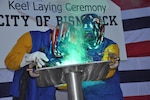 The Honorable Robert O. Wefald (right), former North Dakota State District Court Judge, welds his initials into the keel plate of the future USNS City of Bismarck (EPF 9) with the assistance of Austal USA Class A Welder Richard A. Sinclair (left). The keel authentication ceremony was held Jan. 18 at the Austal USA Shipyard in Mobile, Ala.  