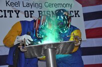 The Honorable Robert O. Wefald (right), former North Dakota State District Court Judge, welds his initials into the keel plate of the future USNS City of Bismarck (EPF 9) with the assistance of Austal USA Class A Welder Richard A. Sinclair (left). The keel authentication ceremony was held Jan. 18 at the Austal USA Shipyard in Mobile, Ala.  