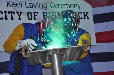 The Honorable Robert O. Wefald (right), former North Dakota State District Court Judge, welds his initials into the keel plate of the future USNS City of Bismarck (EPF 9) with the assistance of Austal USA Class A Welder Richard A. Sinclair (left). The keel authentication ceremony was held Jan. 18 at the Austal USA Shipyard in Mobile, Ala.  