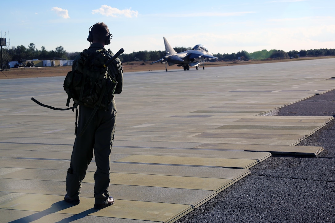 Maj. Aaron Hamblin observes an AV-8B Harrier as the training pilots inside prepare for take-off aboard Marine Corps Auxiliary Landing Field Bogue, N.C., Jan. 18, 2017. Marine Attack Training Squadron 203, Marine Aircraft Group 14, 2nd Marine Aircraft Wing, trains pilots to take-off from, land on and fly in any clime and place, including confined naval ships and spacious airfields. Hamblin is an instructor pilot with VMAT-203. (U.S. Marine Corps photo by Cpl. Mackenzie Gibson/ Released)
