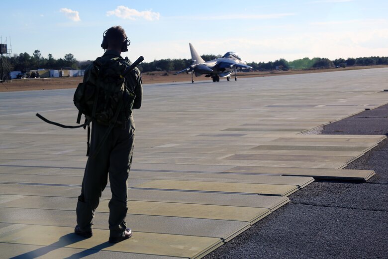 Maj. Aaron Hamblin observes an AV-8B Harrier as the training pilots inside prepare for take-off aboard Marine Corps Auxiliary Landing Field Bogue, N.C., Jan. 18, 2017. Marine Attack Training Squadron 203, Marine Aircraft Group 14, 2nd Marine Aircraft Wing, trains pilots to take-off from, land on and fly in any clime and place, including confined naval ships and spacious airfields. Hamblin is an instructor pilot with VMAT-203. (U.S. Marine Corps photo by Cpl. Mackenzie Gibson/ Released)