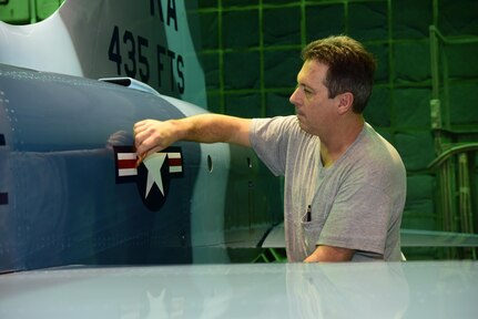 Neil Orlowski, a Corrosion Control Specialist in the 12th Maintenance Group, applies a decal to a T-38C Talon at Joint Base San Antonio-Randolph, Texas, Jan. 13, 2017.  Members of the corrosion control shop are changing the plane’s color scheme from two-tone gray to heritage blue, a scheme that was used by the 435th Fighter Training Squadron 40 years ago, ahead of a reunion of pilots that trained for fighter fundamentals after Jan. 1, 1977. (U.S. Air Force photo/Randy Martin) 