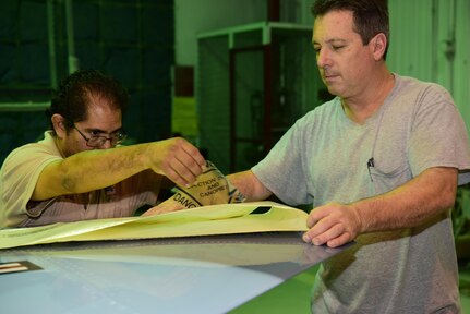 Marion Tarin and Neil Orlowski, both Corrosion Control Specialists in the 12th Maintenance Group, prepare a decal for application paint to a T-38C Talon at Joint Base San Antonio-Randolph, Texas, Jan. 13, 2017. Members of the corrosion control shop are changing the plane’s color scheme from two-tone gray to heritage blue, a scheme that was used by the 435th Fighter Training Squadron 40 years ago, ahead of a reunion of pilots that trained for fighter fundamentals after Jan. 1, 1977. (U.S. Air Force photo/Randy Martin)